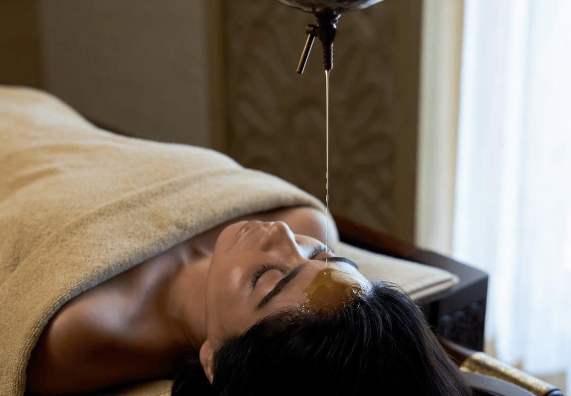 A woman receiving Shirodhara, warm oil streaming steadily onto her forehead