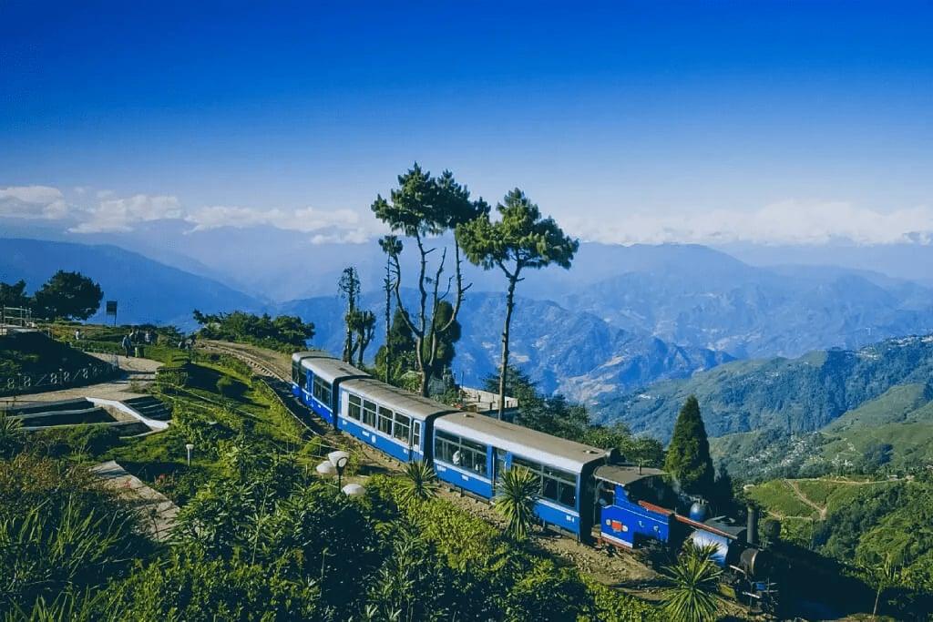 The blue Darjeeling Himalayan Railway toy train curving along a forested hillside
