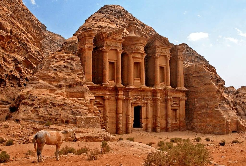 The rock-carved facade of Ad-Deir, the Monastery at Petra, with a horse resting in front